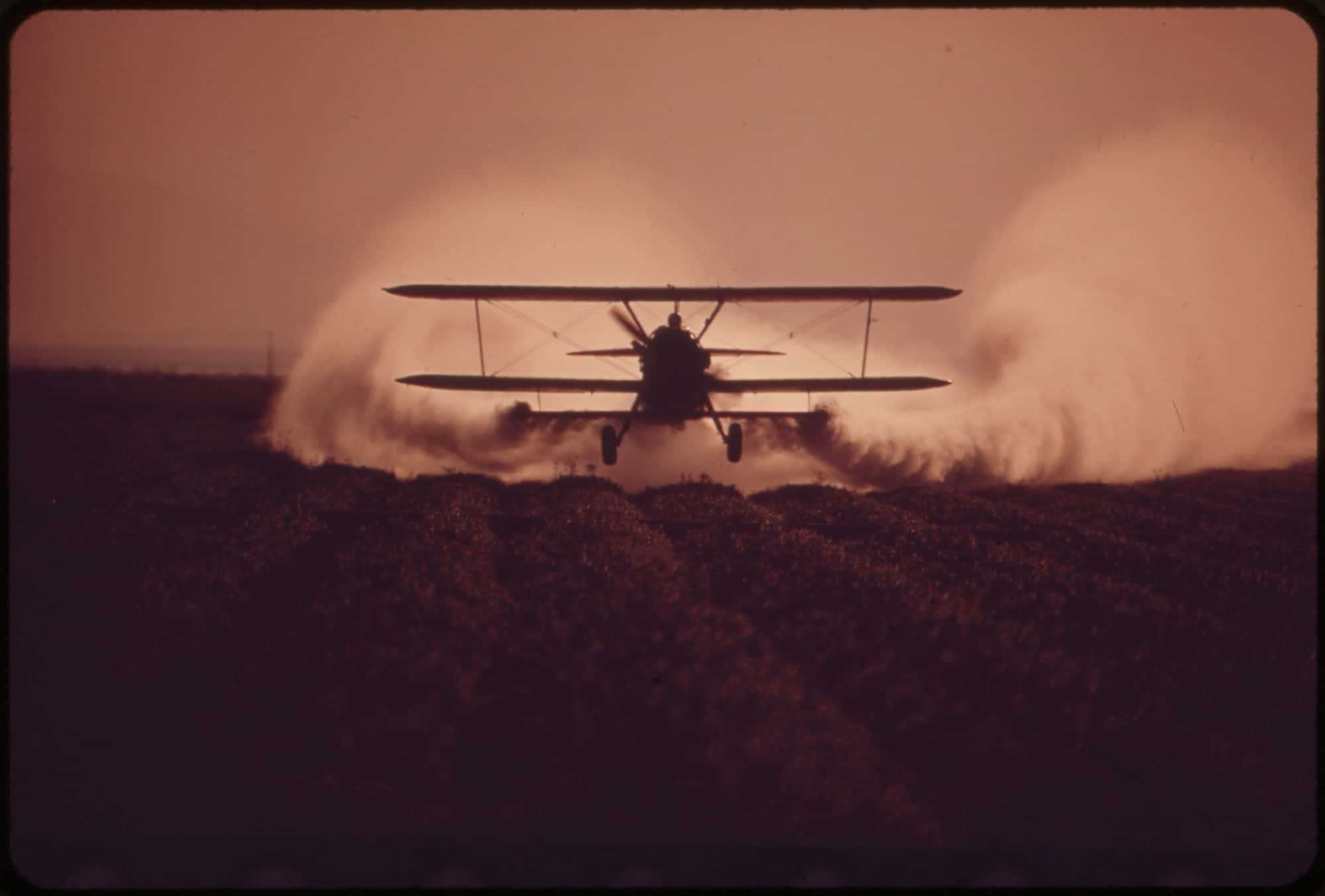 An airplane spraying pesticide over a farm field